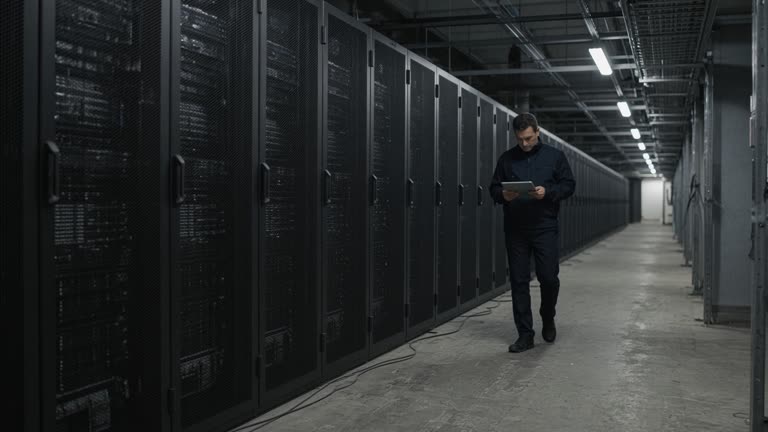 Rows of cloud data-center server racks in a cold aisle under overhead fluorescents, compliance officer with a tablet walking the aisle, scuffed concrete floor and cable trays, no logos or readable text
