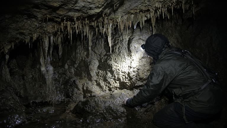 Limestone cave interior with stalactites and a researcher’s headlamp beam on wet rock, cool shadowed tones, no logos or readable text