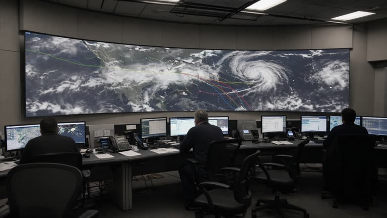 NOAA weather operations floor with curved wall display showing abstract Atlantic storm tracks and analysts at dimly lit workstations, screen details unreadable, no logos