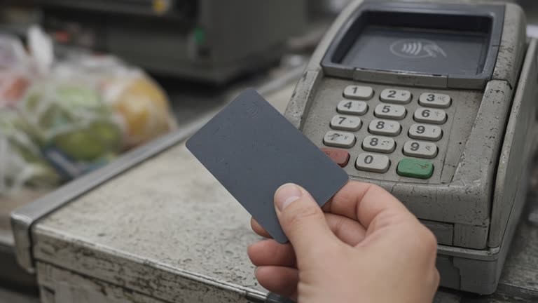 Close-up of a payment terminal keypad and a contactless card tap at a grocery checkout lane under flat fluorescent light, worn plastic and scuffed counter edge, shallow depth of field, no logos or readable text
